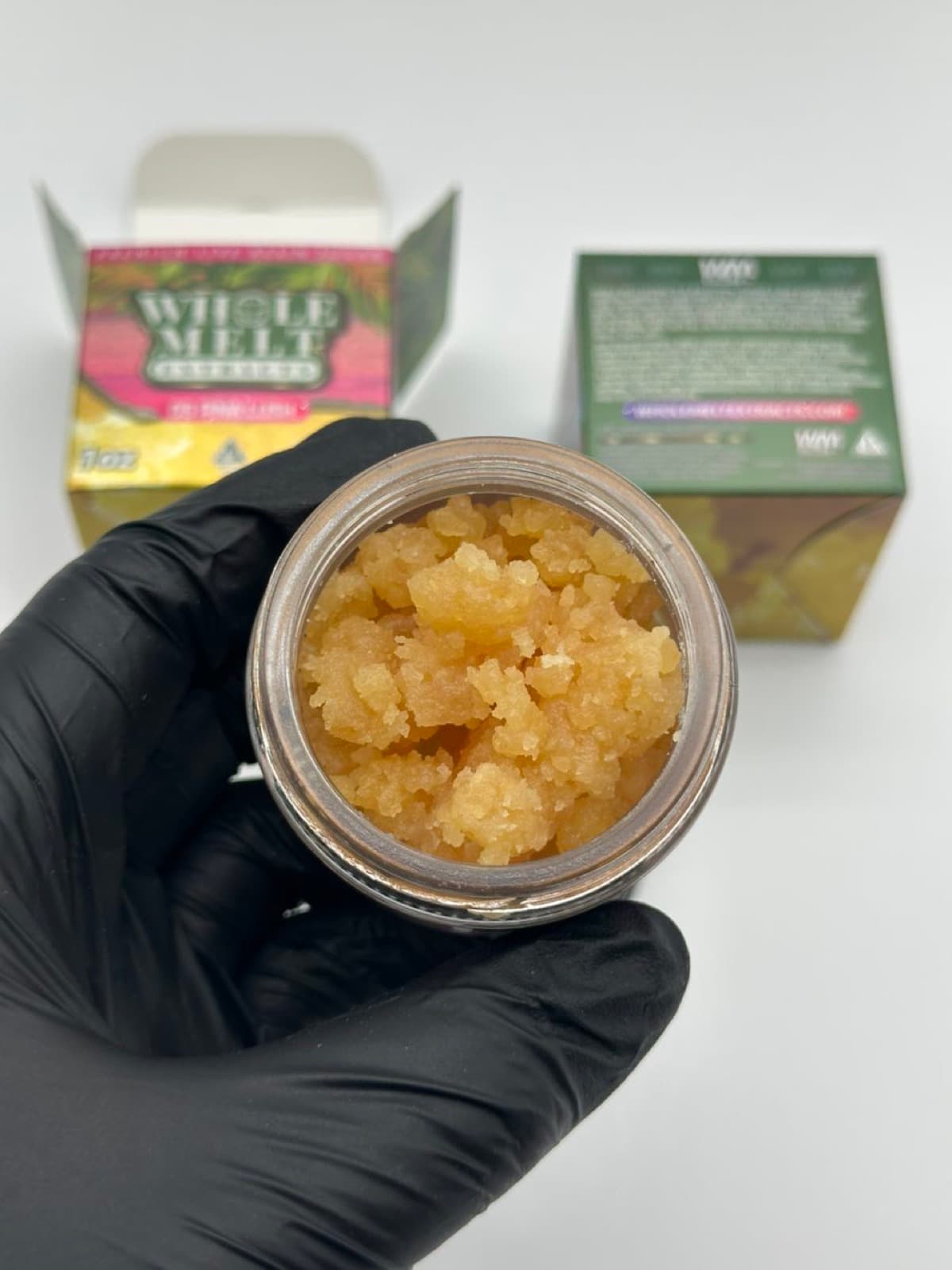 Open jar of golden live resin sugar held in hand